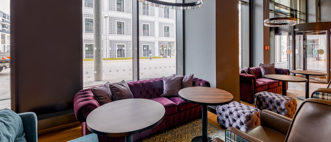 Modern lobby with purple sofas, round tables and large windows overlooking a street. Elegant lighting and a cozy atmosphere., © Premier Inn Modern lobby with purple sofas, round tables and large windows overlooking a street. Elegant lighting and a cozy atmosphere., © Premier Inn