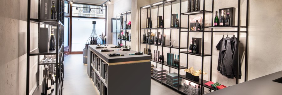 Moderner Laden mit eleganten Regalen, die Flaschen und Geschenkboxen präsentieren. Zentraler Tisch mit weiteren Produkten, helle Beleuchtung., © KESSLER Sekt GmbH & Co. KG