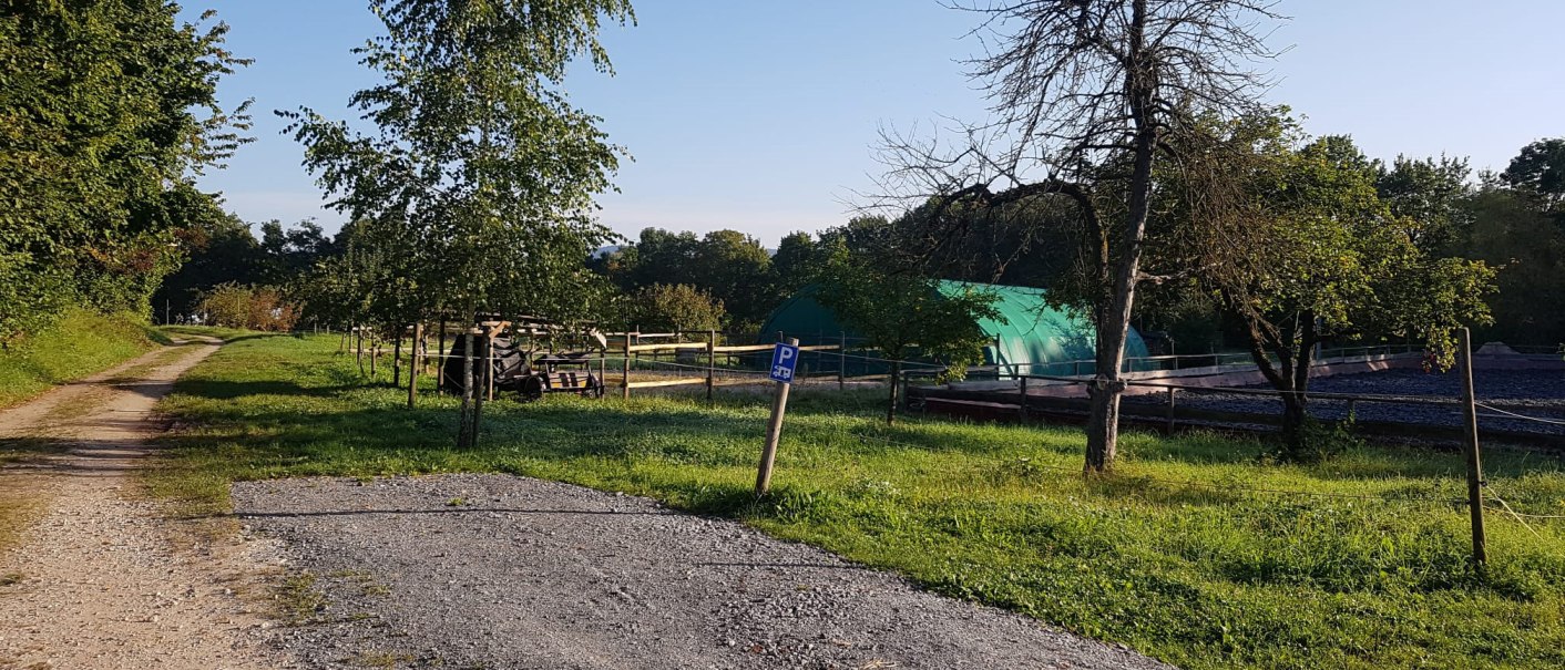 A dirt track leads through a green landscape with trees and a green tent. A sign points to a parking lot., &copy; Mannschreck-Weine