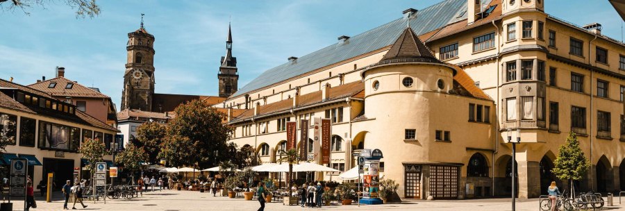 The Markthalle Stuttgart in sunny weather, surrounded by people, bicycles and trees. Historic buildings in the background., © SMG Stuttgart Marketing GmbH - Sarah Schmid