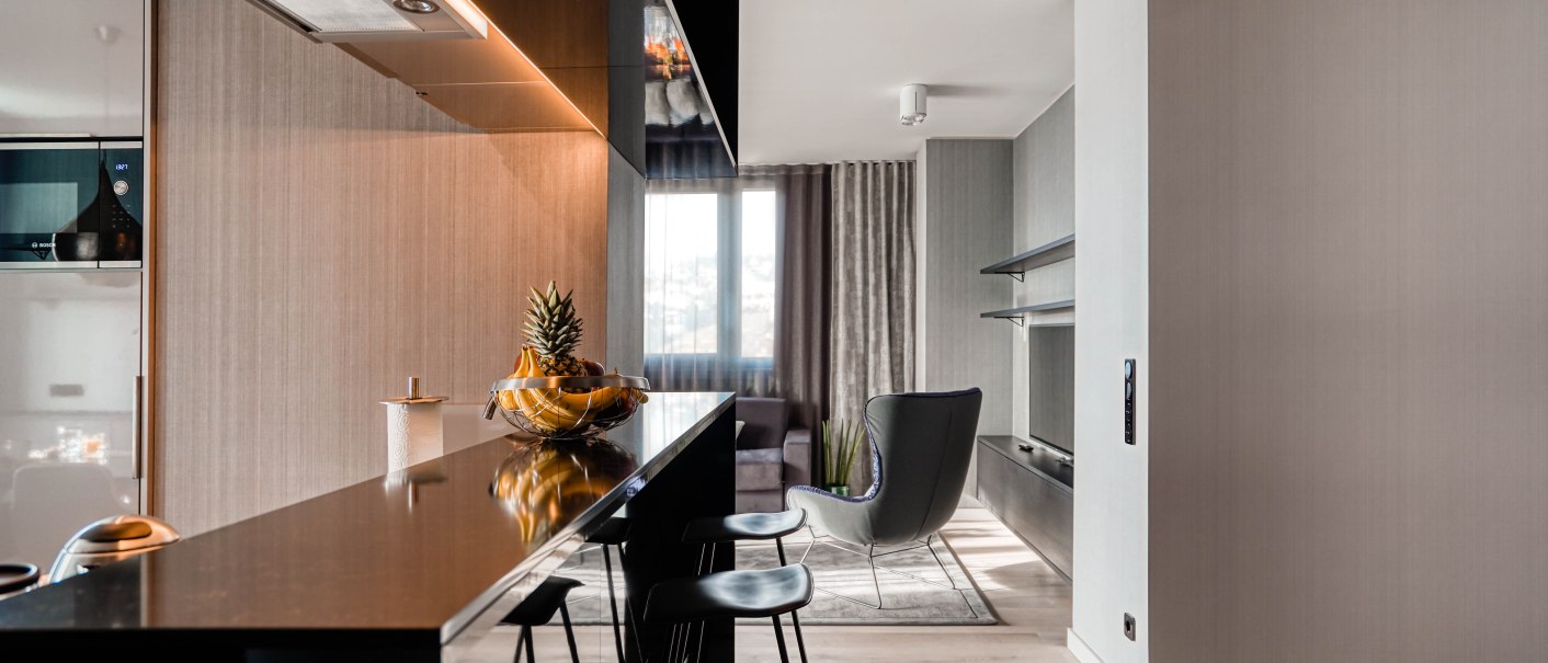Moderne Penthouse-Suite mit stilvoller Küchenzeile, Barhockern und einem gemütlichen Wohnbereich mit Sessel und großem Fenster., © CLOUD N°7 APARTMENTS GmbH Moderne Penthouse-Suite mit stilvoller Küchenzeile, Barhockern und einem gemütlichen Wohnbereich mit Sessel und großem Fenster., © CLOUD N°7 APARTMENTS GmbH