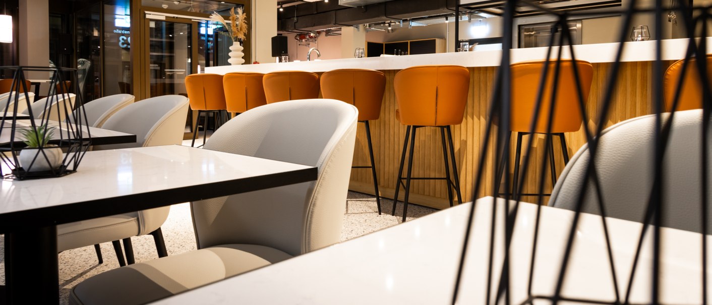 Moderne Bar mit weißen Tischen, orangefarbenen Barhockern und stilvoller Dekoration. Industrielles Design mit sichtbaren Rohren an der Decke., © GINN Apartments Esslingen Moderne Bar mit weißen Tischen, orangefarbenen Barhockern und stilvoller Dekoration. Industrielles Design mit sichtbaren Rohren an der Decke., © GINN Apartments Esslingen
