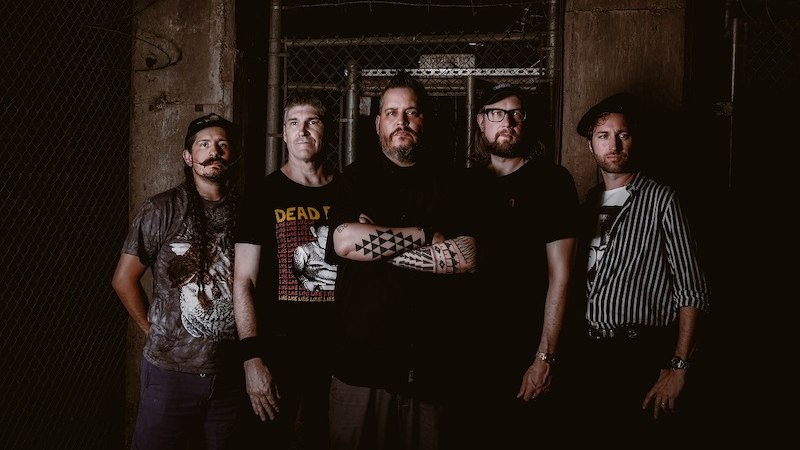 Fünf Männer posieren vor einem dunklen, industriellen Hintergrund. Einer trägt ein T-Shirt mit der Aufschrift 'DEAD PIONEERS'., © Jugendhaus West Fünf Männer posieren vor einem dunklen, industriellen Hintergrund. Einer trägt ein T-Shirt mit der Aufschrift 'DEAD PIONEERS'., © Jugendhaus West