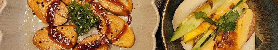 A plate of vegan dumplings in sauce, a bao bun with vegetables and a drink with ice cubes on a wooden table., © SMG A plate of vegan dumplings in sauce, a bao bun with vegetables and a drink with ice cubes on a wooden table., © SMG