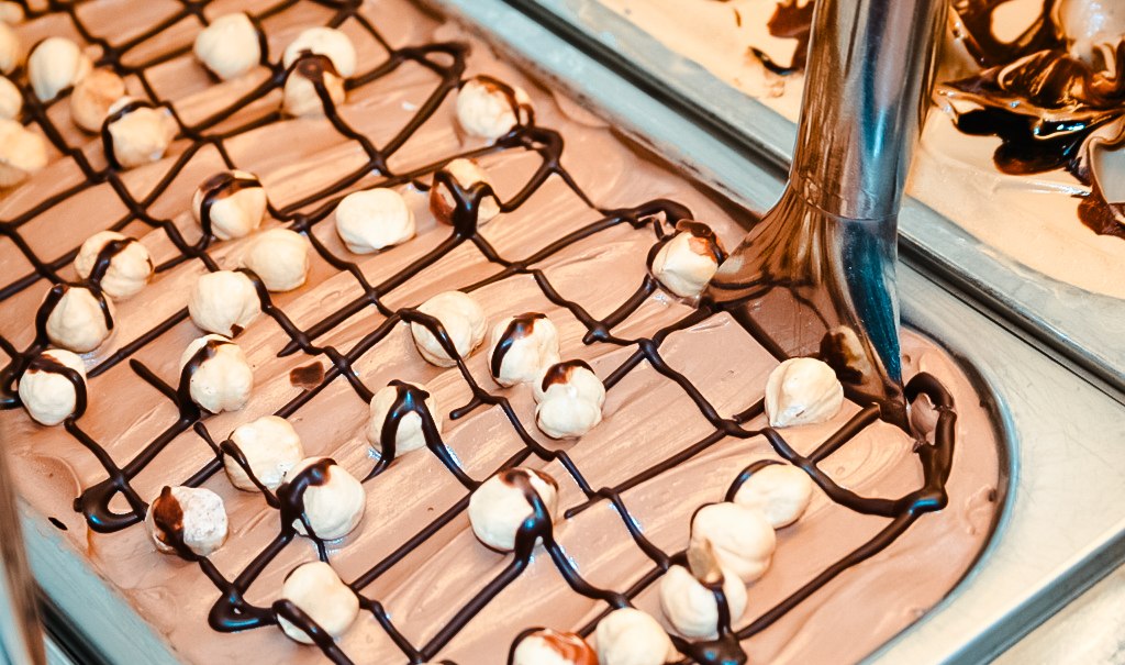 Haselnusseis mit Schokoladensauce und ganzen Haselnüssen in einer Eisschale. Eine Eisschaufel ist zu sehen., © Old Bridge Gelateria Stuttgart Haselnusseis mit Schokoladensauce und ganzen Haselnüssen in einer Eisschale. Eine Eisschaufel ist zu sehen., © Old Bridge Gelateria Stuttgart