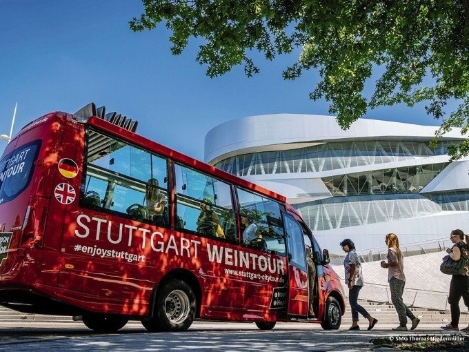 Roter Bus der Stuttgart Weintour vor einem modernen Geb&auml;ude. Menschen gehen vorbei, B&auml;ume spenden Schatten., &copy; SMG, Thomas Niederm&uuml;ller