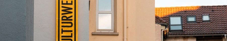 A yellow sign with the inscription 'KULTURWERK' hangs on the wall of a house. Next to it is a window and a clock., © SMG Stuttgart Marketing GmbH - Sarah Schmid A yellow sign with the inscription 'KULTURWERK' hangs on the wall of a house. Next to it is a window and a clock., © SMG Stuttgart Marketing GmbH - Sarah Schmid