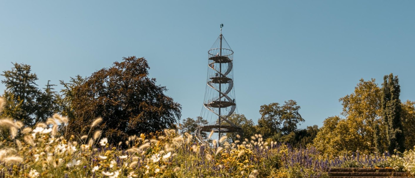 Der Killesbergturm ragt über bunte Blumen und Bäume in einem Park in den blauen Himmel., © Stuttgart-Marketing GmbH, Sarah Schmid