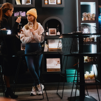 Two women in a stylish caf&eacute;, one with a yellow cap, holding glasses of wine. Shelves with products and a fridge can be seen in the background., &copy; Stuttgart-Marketing GmbH, Alwin Maigler