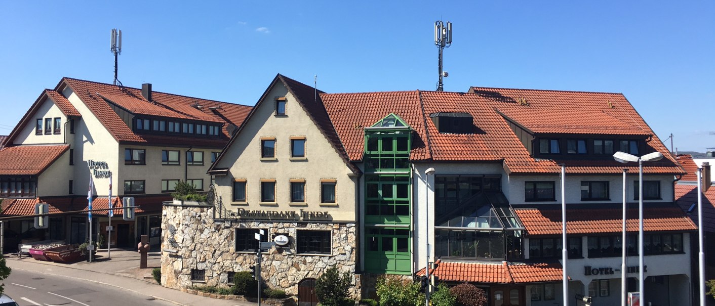 Das Neo Hotel Linde in Esslingen mit roten Ziegeldächern und grünen Fenstern, umgeben von einer Straße und unter blauem Himmel., © TOMAS