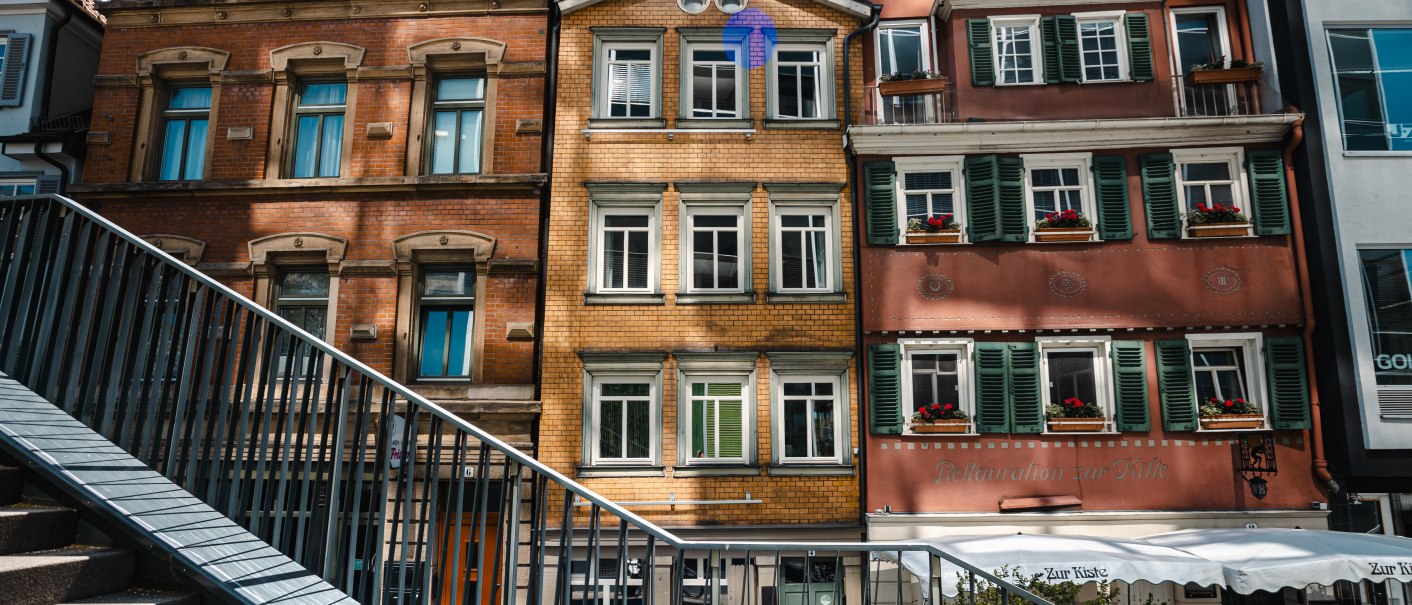 Drei bunte historische Gebäude mit Fensterläden, davor eine Treppe mit Geländer. Die Fassaden sind rot, gelb und rosa. Sonniger Tag., © SMG Stuttgart Marketing GmbH - Sarah Schmid