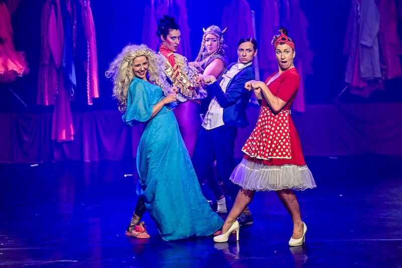 Five women in colorful costumes pose on a stage. They wear eye-catching outfits and stand in a dynamic pose., © Theaterhaus Stuttgart e.V. Five women in colorful costumes pose on a stage. They wear eye-catching outfits and stand in a dynamic pose., © Theaterhaus Stuttgart e.V.