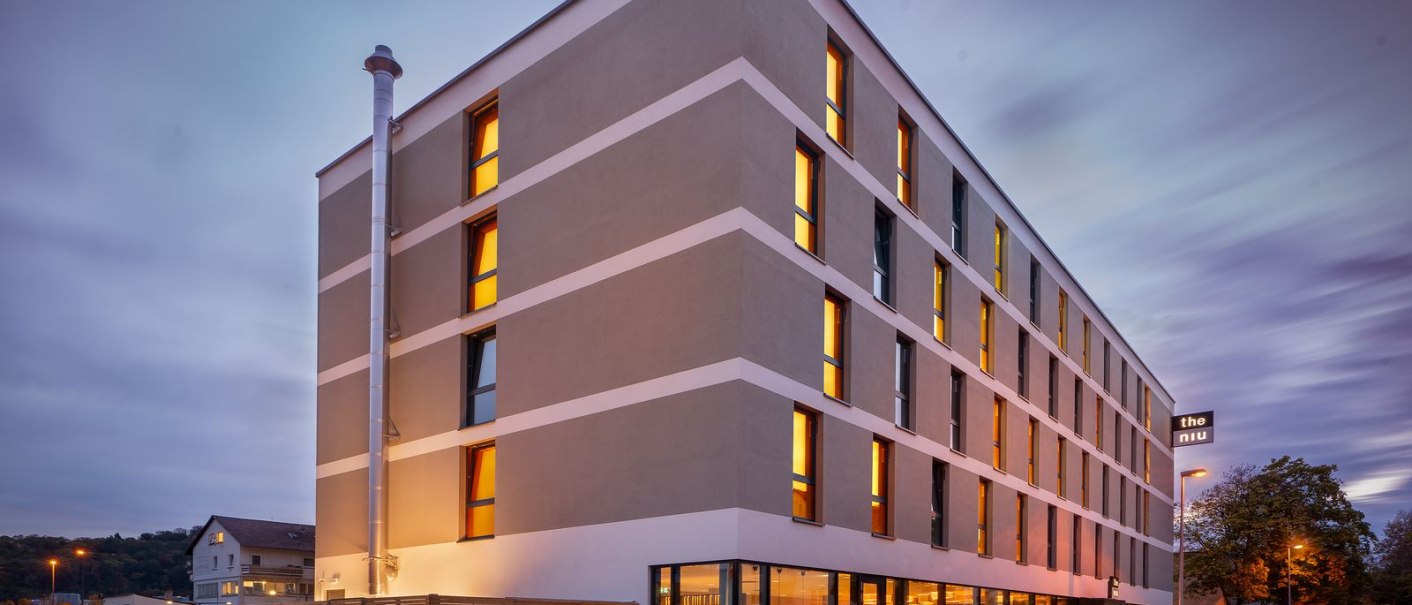 Moderne Hotelaußenfassade bei Dämmerung, beleuchtete Fenster, Schild mit 'the niu'., © Novum Hospitality