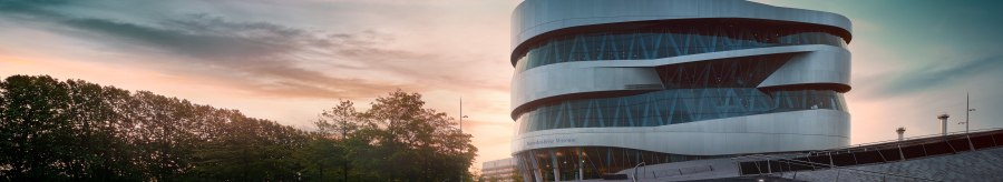 Das Mercedes-Benz Museum in Stuttgart bei Sonnenuntergang. Moderne Architektur mit geschwungenen Linien, umgeben von Bäumen und beleuchteten Stufen., © Mercedes-Benz Heritage GmbH