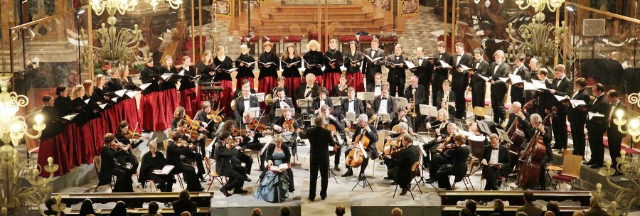 Ein Orchester und Chor in einer prunkvollen Kapelle führen ein Konzert auf. Der Dirigent steht vor den Musikern, während das Publikum zuschaut., © Konrad Eichbichler