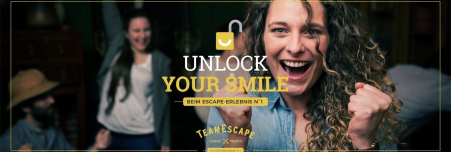 Woman cheering with clenched fists, other people celebrating in the background. Text: "Unlock Your Smile" and "TeamEscape"., © TeamEscape Stuttgart Woman cheering with clenched fists, other people celebrating in the background. Text: "Unlock Your Smile" and "TeamEscape"., © TeamEscape Stuttgart
