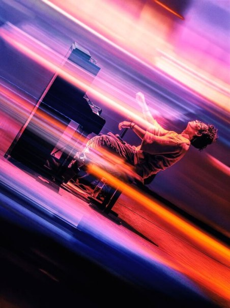 A musician plays the piano on a stage, surrounded by dynamic lighting effects in vibrant colors. The scene radiates energy and movement., &copy; Theaterhaus Stuttgart e.V.