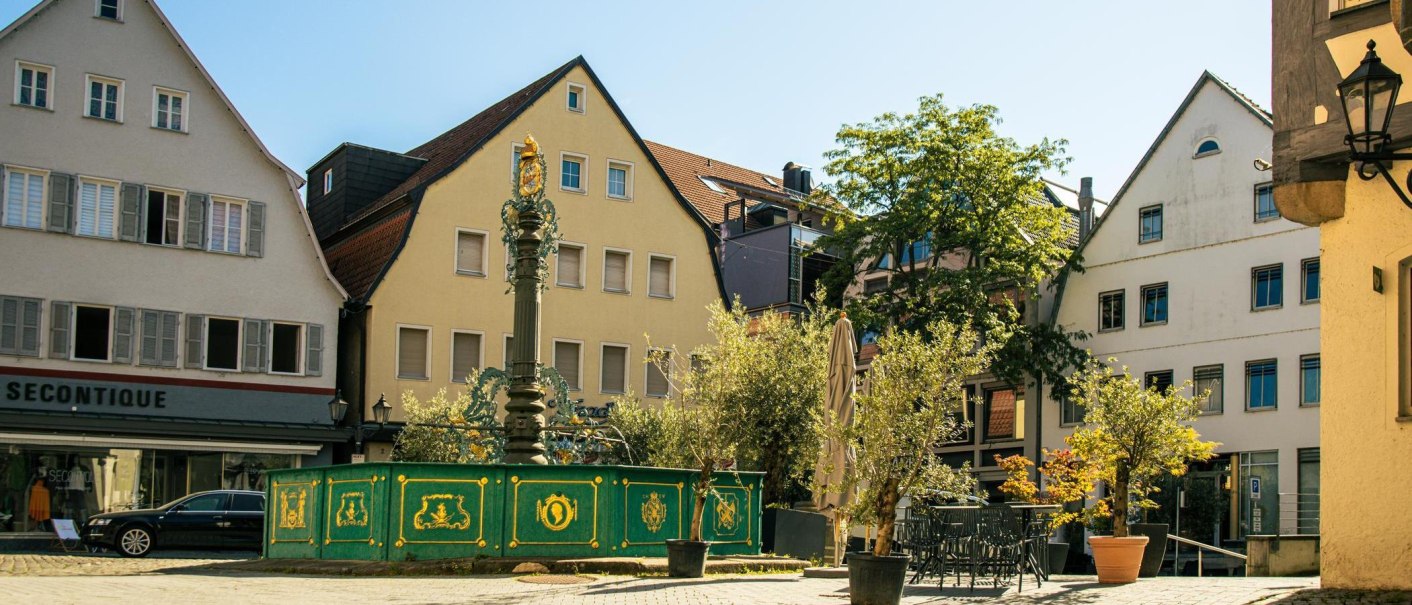 The market square in Nürtingen shows a historic fountain surrounded by half-timbered houses and trees under a clear sky., © Stuttgart-Marketing GmbH, Sarah Schmid The market square in Nürtingen shows a historic fountain surrounded by half-timbered houses and trees under a clear sky., © Stuttgart-Marketing GmbH, Sarah Schmid