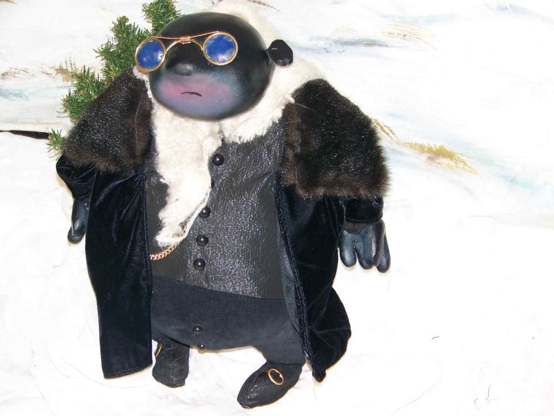 Eine Maulwurf-Figur trägt elegante Kleidung und eine Sonnenbrille, steht vor einem schneebedeckten Hintergrund mit Tannen. Stilvoll und winterlich gekleidet., © Nellys Puppentheater Eine Maulwurf-Figur trägt elegante Kleidung und eine Sonnenbrille, steht vor einem schneebedeckten Hintergrund mit Tannen. Stilvoll und winterlich gekleidet., © Nellys Puppentheater