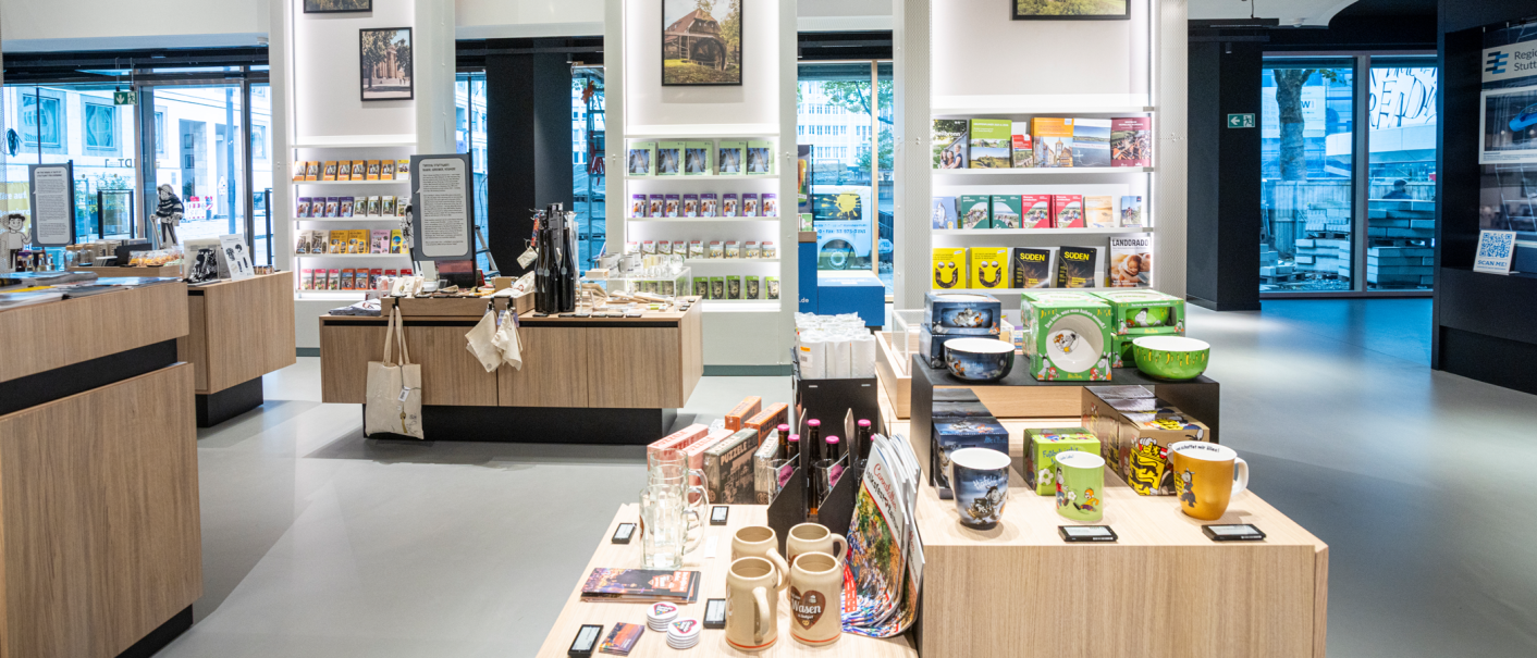 Modern souvenir shop with wooden shelves filled with books, mugs and regional products. Large windows offer a view outside., © Stuttgart-Marketing GmbH, Sarah Schmid Modern souvenir shop with wooden shelves filled with books, mugs and regional products. Large windows offer a view outside., © Stuttgart-Marketing GmbH, Sarah Schmid