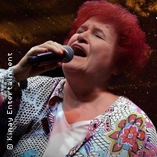 Frau mit rotem Haar singt leidenschaftlich in ein Mikrofon vor einem dunklen Hintergrund., &copy; links im Bild