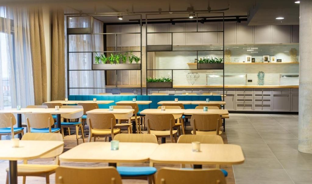 Modern dining room with wooden tables and blue chairs. Plants and shelves can be seen in the background. Bright, inviting atmosphere., © Arthotel ANA Momentum Modern dining room with wooden tables and blue chairs. Plants and shelves can be seen in the background. Bright, inviting atmosphere., © Arthotel ANA Momentum