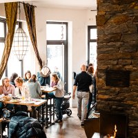 Cosy caf&eacute; with large windows, people at tables, colorful baubles on the wall and a fireplace. Warm, inviting atmosphere., &copy; SMG, Sarah Schmid