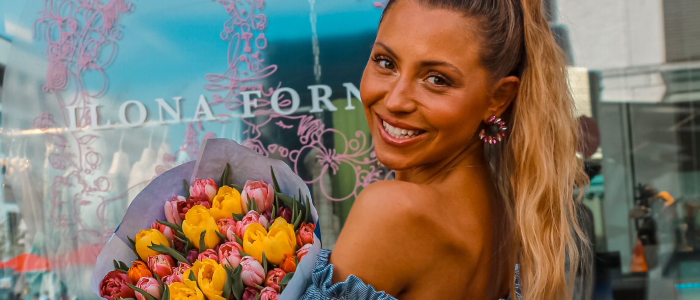Frau mit Blumenstrauß lächelt vor einem Schaufenster mit dem Schriftzug 'Ilona Forner'., © Ilona Forner, Stuttgart Frau mit Blumenstrauß lächelt vor einem Schaufenster mit dem Schriftzug 'Ilona Forner'., © Ilona Forner, Stuttgart