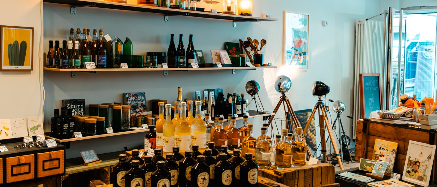 Ein gemütlicher Laden mit Regalen voller Flaschen, Lampen und Dekorationsartikeln. Holzkisten und Tripod-Lampen ergänzen das Ambiente., © SMG_Sarah Schmid