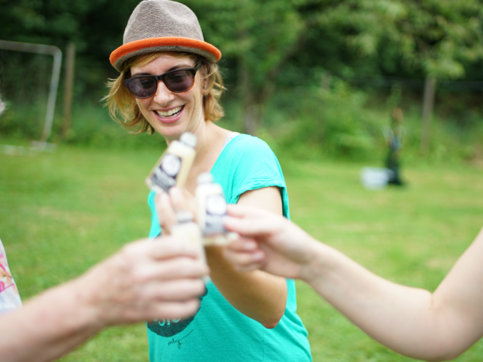 A person in a hat and sunglasses clinks glasses with other small bottles outside. Everyone seems cheerful., © Cool-Tours StattReisen A person in a hat and sunglasses clinks glasses with other small bottles outside. Everyone seems cheerful., © Cool-Tours StattReisen