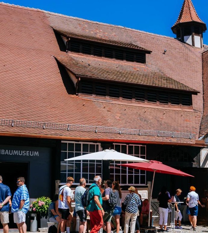 Visitors stand in front of the wine museum in Uhlbach. The half-timbered building has a red tiled roof. Vineyards can be seen in the background., © Stuttgart-Marketing GmbH, Thomas Niedermüller