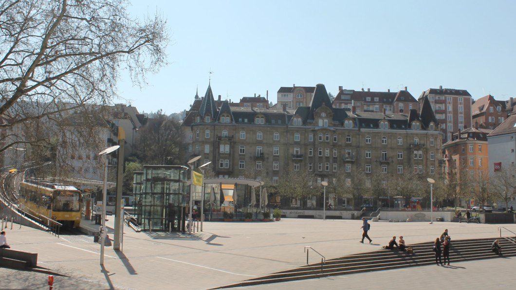 Marienplatz in Stuttgart mit Straßenbahn, modernen und historischen Gebäuden. Menschen sitzen auf Treppen, Bäume ohne Laub, sonniger Tag., © Stuttgart-Marketing GmbH Marienplatz in Stuttgart mit Straßenbahn, modernen und historischen Gebäuden. Menschen sitzen auf Treppen, Bäume ohne Laub, sonniger Tag., © Stuttgart-Marketing GmbH