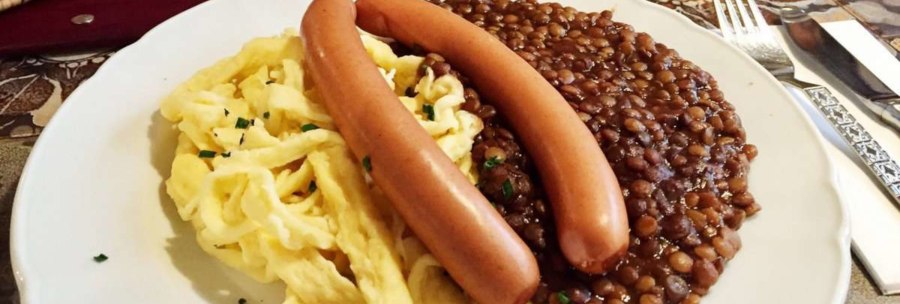Ein Teller mit Linsen, Spätzle und zwei Würstchen, serviert auf einem Tisch mit Besteck., © TMBW, Susi Maier