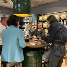 Group of people standing around a table in a store. Barrels can be seen in the background. The atmosphere is sociable and relaxed., © links im Bild Group of people standing around a table in a store. Barrels can be seen in the background. The atmosphere is sociable and relaxed., © links im Bild
