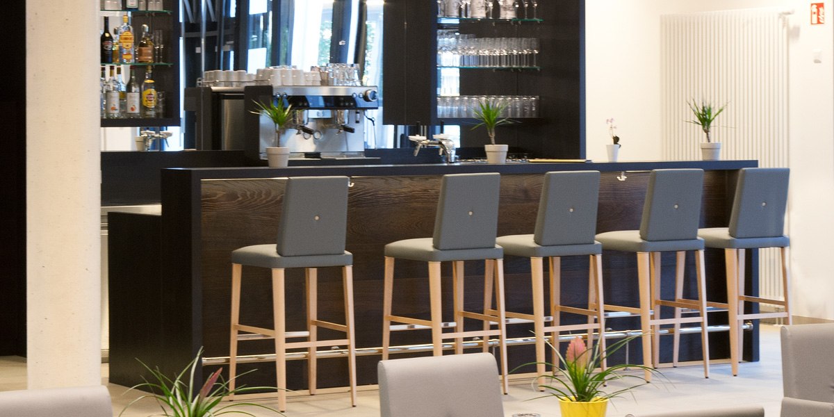 Moderne Bar mit hohen Stühlen, Espressomaschine und Regalen mit Gläsern und Flaschen. Pflanzen dekorieren die Theke., © Star Inn Stuttgart Airport-Messe Moderne Bar mit hohen Stühlen, Espressomaschine und Regalen mit Gläsern und Flaschen. Pflanzen dekorieren die Theke., © Star Inn Stuttgart Airport-Messe