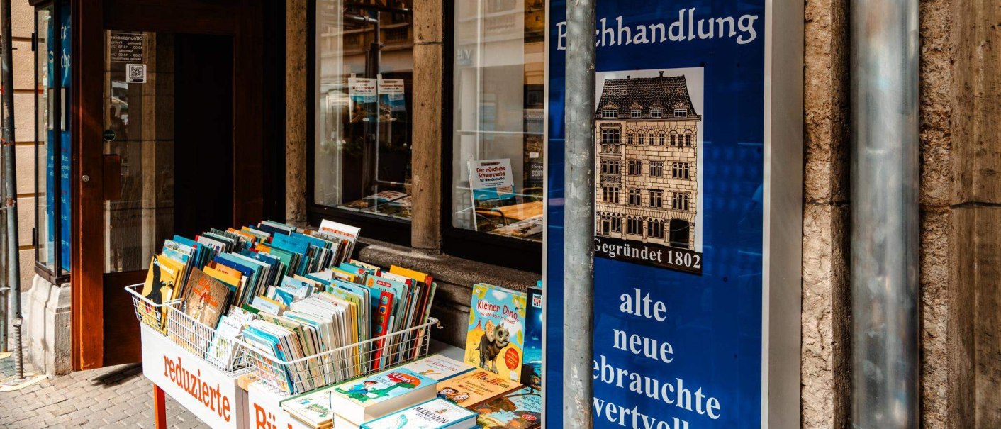 Antiquariat mit B&uuml;cherkiste vor dem Eingang, Schaufenster mit Plakaten und einem Schild mit der Aufschrift 'Gegr&uuml;ndet 1802'. B&uuml;cher zum Verkauf ausgestellt., &copy; Stuttgart-Marketing GmbH, Sarah Schmid