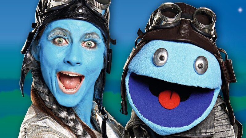 Zwei Figuren mit blauer Haut und Fliegerbrillen lächeln vor einem Sternenhimmel. Eine ist eine Puppe, die andere eine Person., © Theaterhaus Stuttgart e.V.