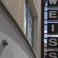 Ein Schild mit der Aufschrift 'WEISS' h&auml;ngt an einem Geb&auml;ude. Der Himmel ist blau mit einigen Wolken. Im Hintergrund sind D&auml;cher zu sehen., &copy; SMG, Sarah Schmid