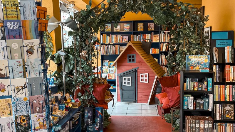 Bookshop with playhouse, plants and shelves full of books and games. Colorful postcards and games are also on display., © Naseweis, Stuttgart Bookshop with playhouse, plants and shelves full of books and games. Colorful postcards and games are also on display., © Naseweis, Stuttgart