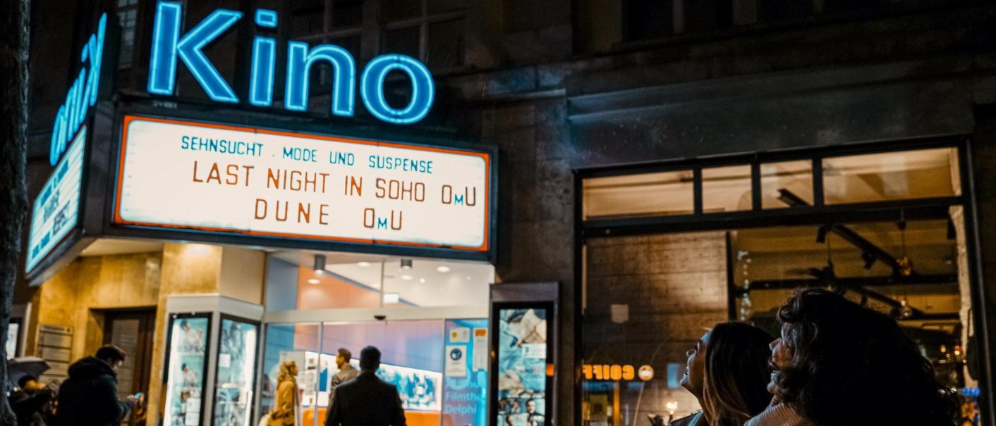 Eingang eines Kinos bei Nacht mit leuchtendem Schild. Menschen stehen davor und schauen nach oben. Filme: 'Last Night in Soho', 'Dune'., © SMG, Alwin Maigler Eingang eines Kinos bei Nacht mit leuchtendem Schild. Menschen stehen davor und schauen nach oben. Filme: 'Last Night in Soho', 'Dune'., © SMG, Alwin Maigler
