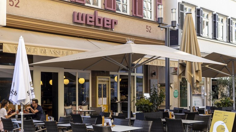 Ein Caf&eacute; mit dem Namen 'Weber' hat einen Au&szlig;enbereich mit Tischen, St&uuml;hlen und Sonnenschirmen. Menschen sitzen und genie&szlig;en Getr&auml;nke., &copy; SMG, Sarah Schmid