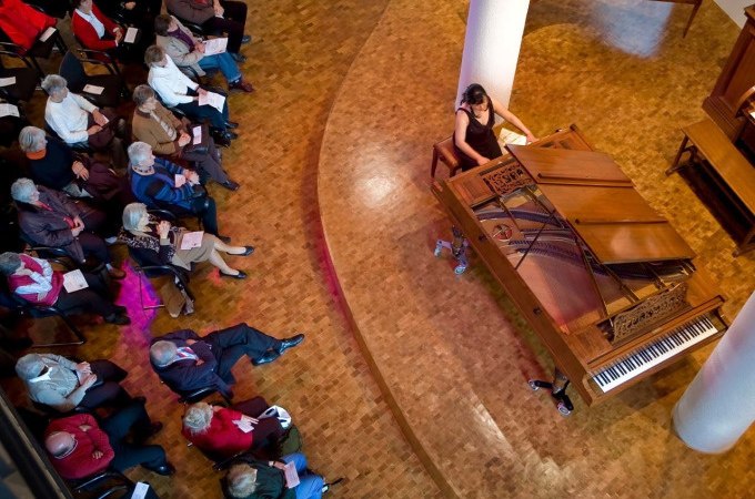 Eine Frau spielt Klavier in einem Konzertsaal, während ein Publikum aufmerksam zuhört. Die Szene ist aus der Vogelperspektive aufgenommen., © Landesmuseum Württemberg