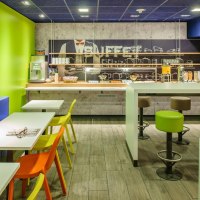 Ein modernes Frühstücksbuffet mit bunten Stühlen, grünen Wänden und einer Auswahl an Speisen und Getränken., © ibis budget Stuttgart City Nord
