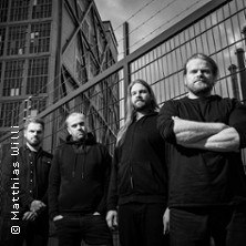 Four men pose in front of a fence in an urban setting. The picture is in black and white and conveys a gloomy mood., &copy; links im Bild