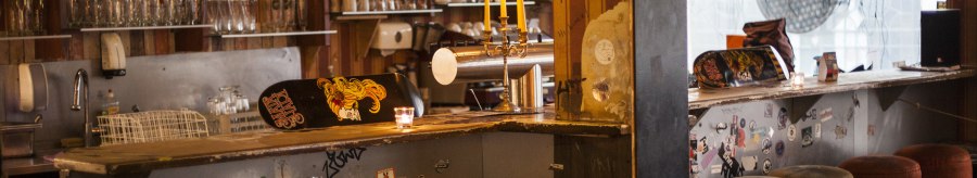 A cozy bar with skateboard decor on the counter, candlesticks and bar stools. Bottles and glasses can be seen in the background., © Mata Hari, Stuttgart