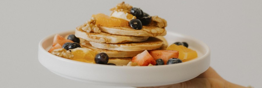 A plate of pancakes, garnished with berries, walnuts and pieces of fruit, is presented by one hand., &copy; sina fotografie, Caf&eacute; Lesbar, Stuttgart