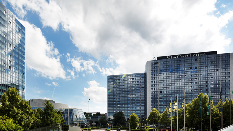 Moderne Gebäude des SI-Centrums mit Glasfassaden, umgeben von Bäumen, unter einem blauen Himmel mit Wolken., © Susanne Wegner Photography