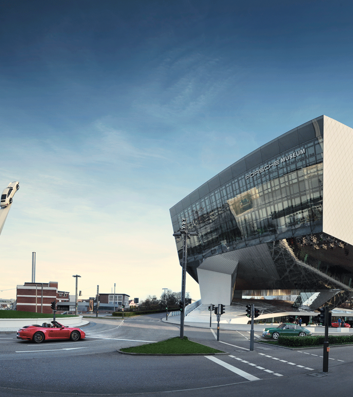 The Porsche Museum in Stuttgart with its futuristic architecture and a sculpture of three cars on tall pillars against a blue sky., &copy; Porsche AG
