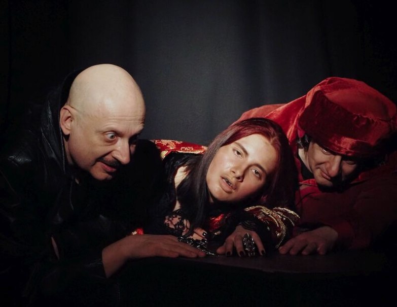 Drei Personen posieren in dunkler Umgebung. Eine tr&auml;gt ein rotes Gewand, eine hat eine Glatze, die dritte hat lange Haare und dunkle Kleidung., &copy; Theater Atelier