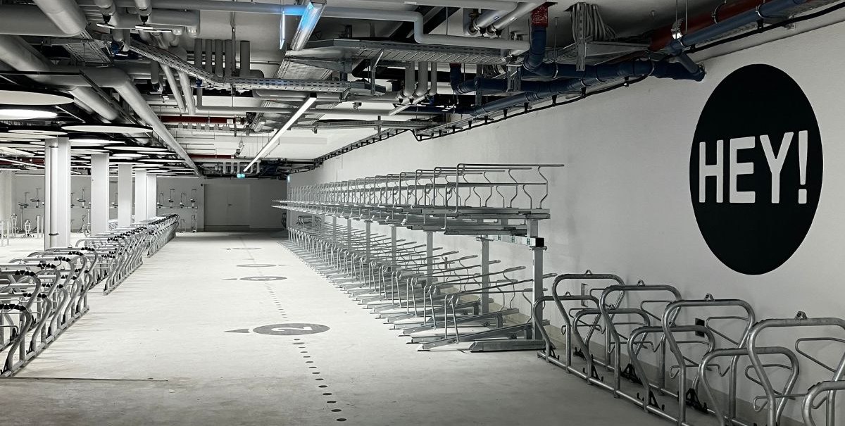 Empty bicycle storage room with metal racks, white walls and the lettering 'HEY!' on the wall., © Stadt Esslingen am Neckar